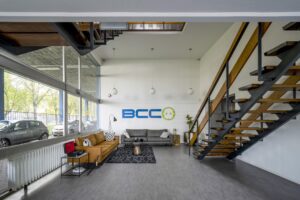 Modern ingerichte wachtruimte met zithoek, open trap en het BCC-logo aan de muur bij Van der Madeweg.